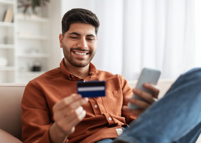 Smiling Arab guy using phone and credit card at home