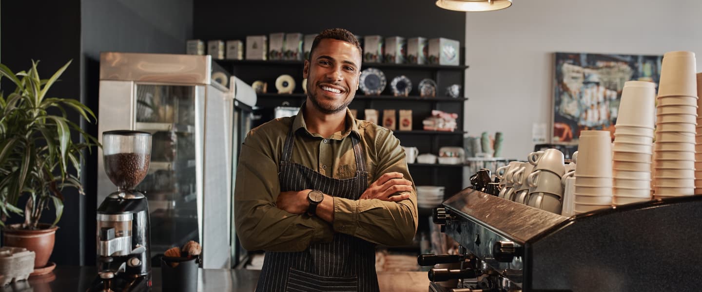 Smiling African man barista standing behind the counter at the coffee shop